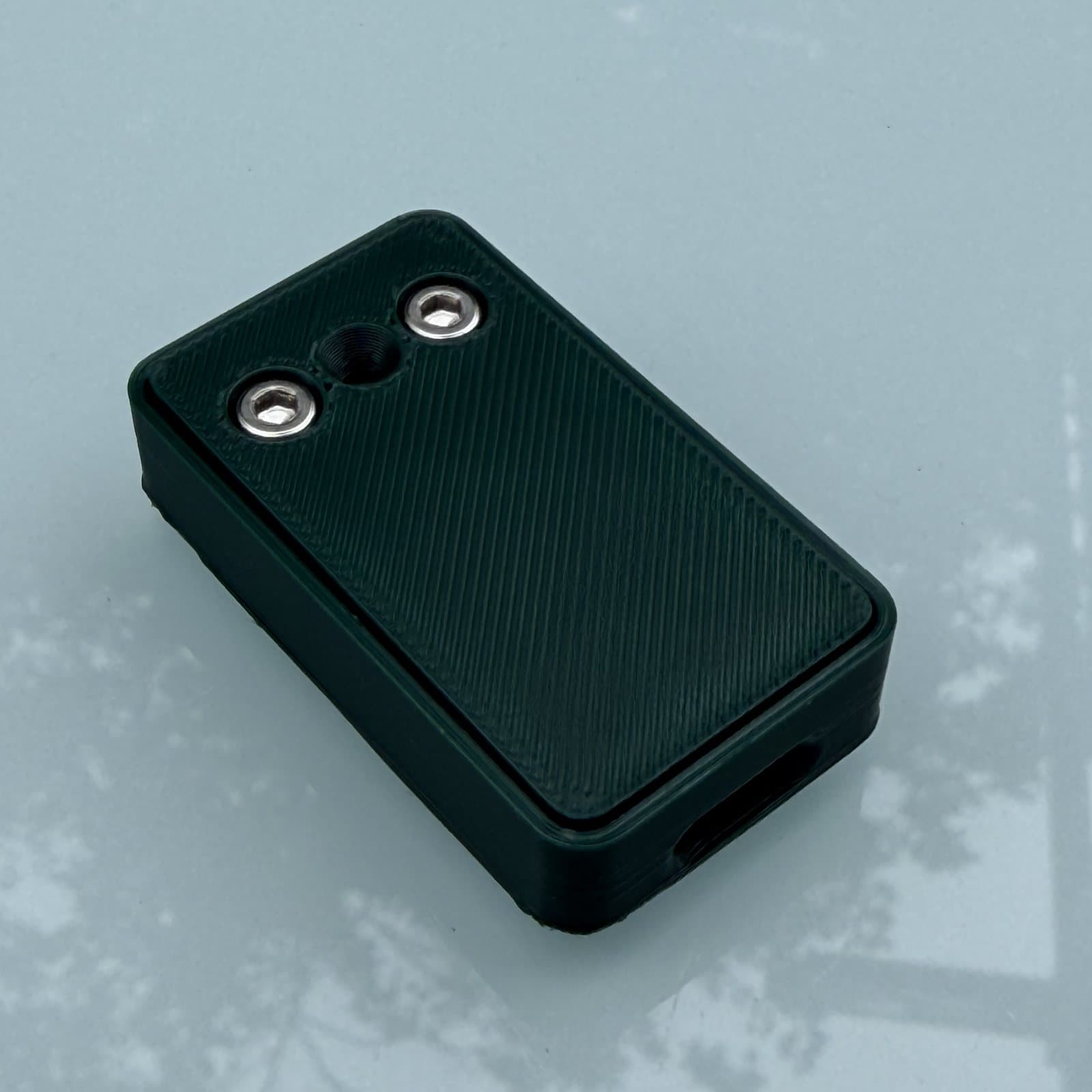 The bat dongle on a pale table: a small dark green rectangular case with a ribbed top, two screw heads and the microphone opening at one end, and a USB-C port at the other.