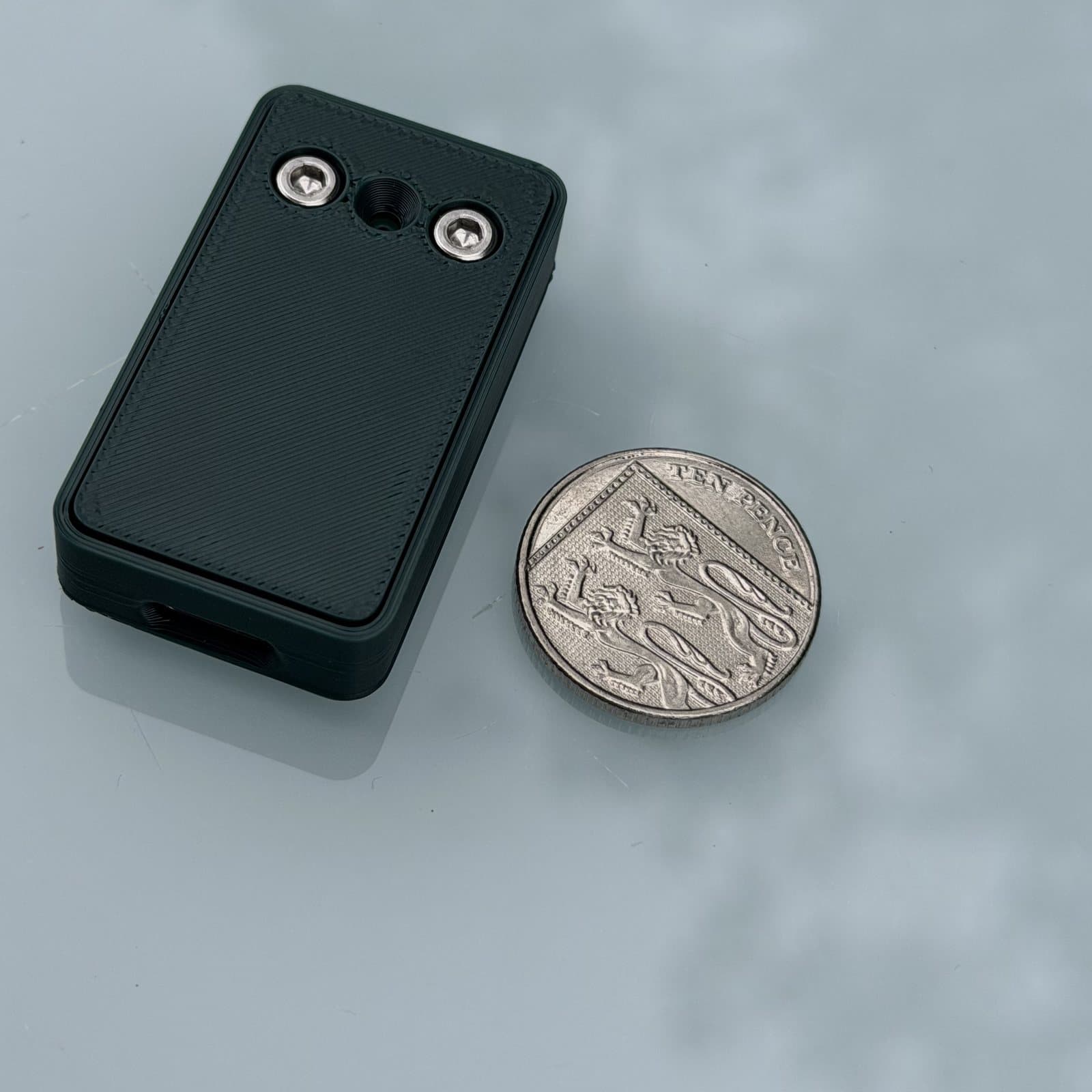 The bat dongle next to a ten pence coin. The dongle is about twice the length of the coin and a little narrower than it.